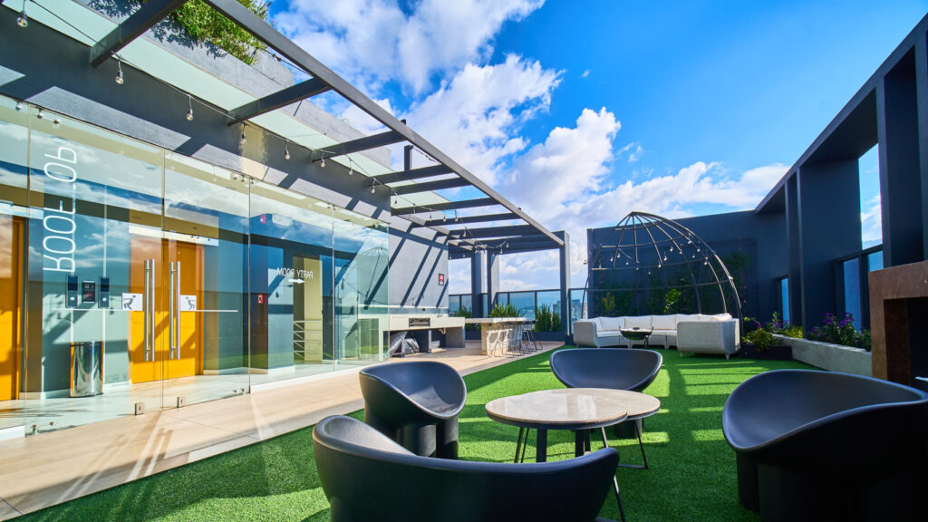 Terraza rooftop con césped y zona lounge de un edificio moderno en Quito bajo cielo azul