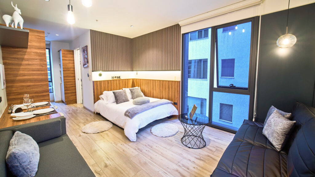 Suite urbana en Quito con cama matrimonial, piso de madera y ventanales hacia la ciudad